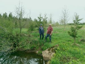 PEI ALUS participant Dan MacLean (right) and Cathy Gallant, Executive Director of the Richmond Bay Watershed Association (left) stand on the bank of the Trout River (Tyne Valley) on Dhachaidh Farms, PEI. ALUS helped expand the riparian zone along the stream, and the Watershed Association helped reforest it. This ALUS project now serves as a wonderful forested wildlife corridor and an effective riparian buffer, keeping the river healthy for future generations. (Photo: Shawn Hill)