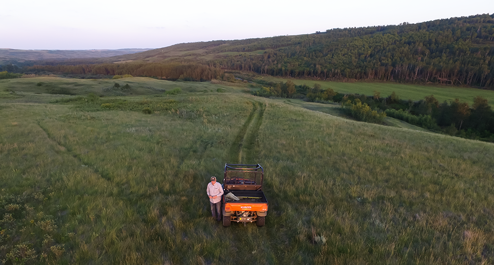 Farmer stands beside vehicle in the middle of a field.